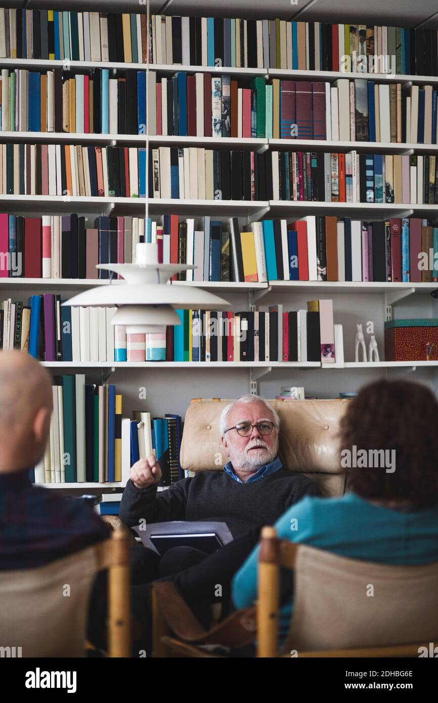 Senior therapist explaining couple while sitting against bookshelf Stock Photo