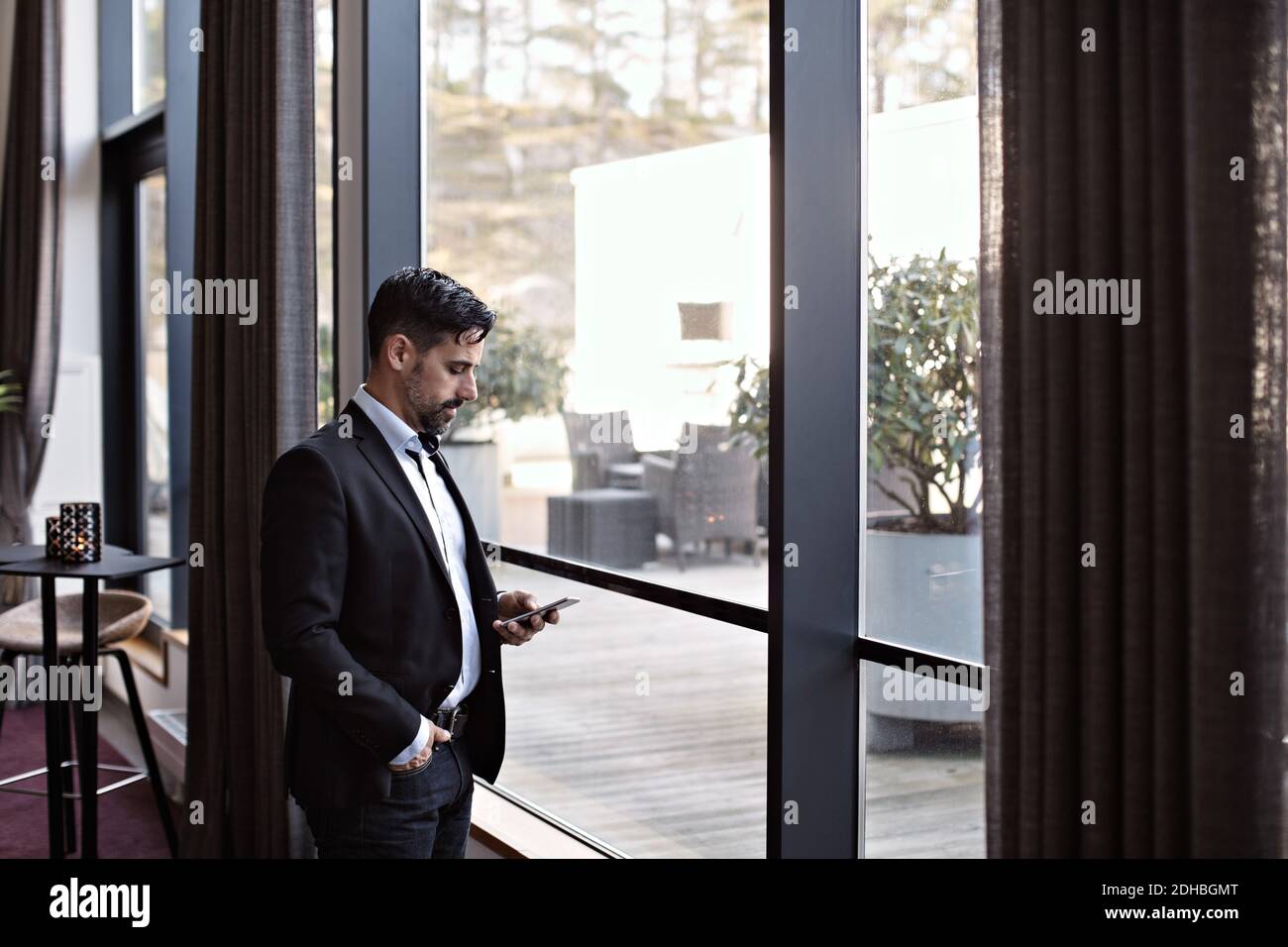 Businessman using phone while standing by window in office Stock Photo