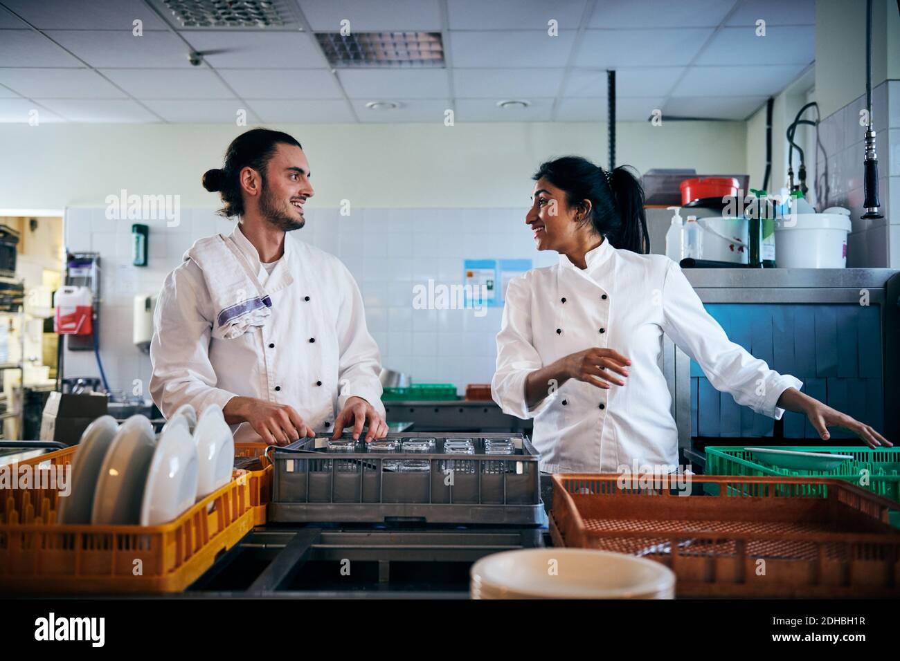 Male and female chefs communicating while arranging utensils in kitchen ...