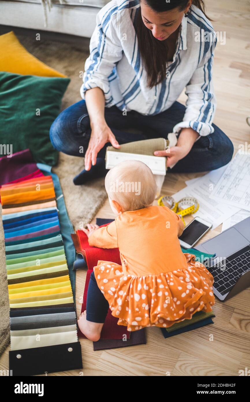 High angle view of female creative professional working while loving daughter playing with fabric swatch on hardwood flo Stock Photo
