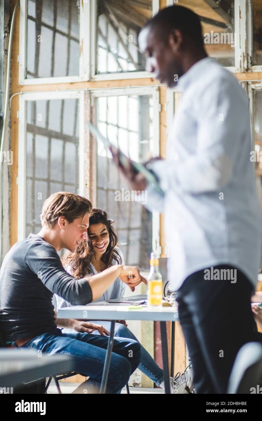Smiling computer programmers using laptop while businessman standing in foreground at creative office Stock Photo