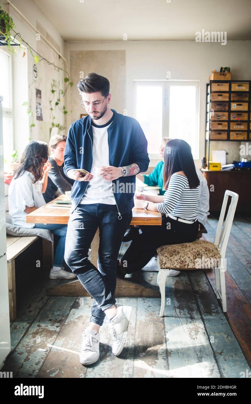 Businessman using smart phone while computer programmers having meeting at workplace Stock Photo