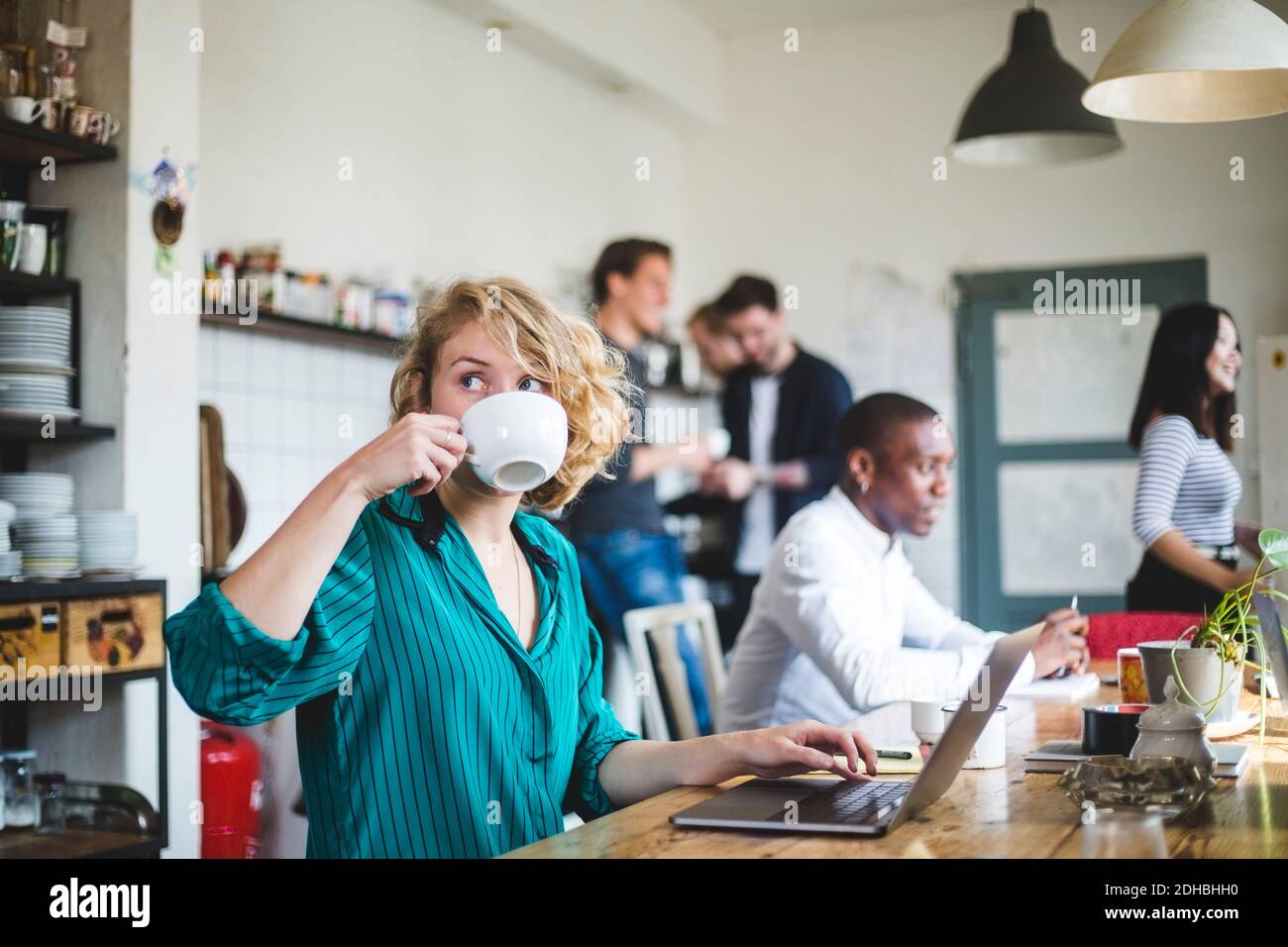 Young businesswoman drinking coffee while computer programmers working in background at office Stock Photo