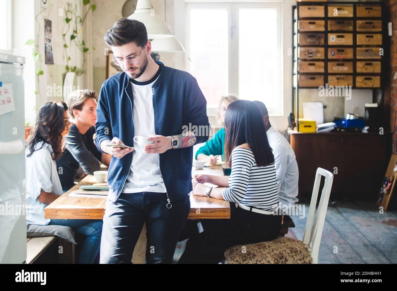 Young male professional using smart phone while IT programmers having meeting at desk in office Stock Photo