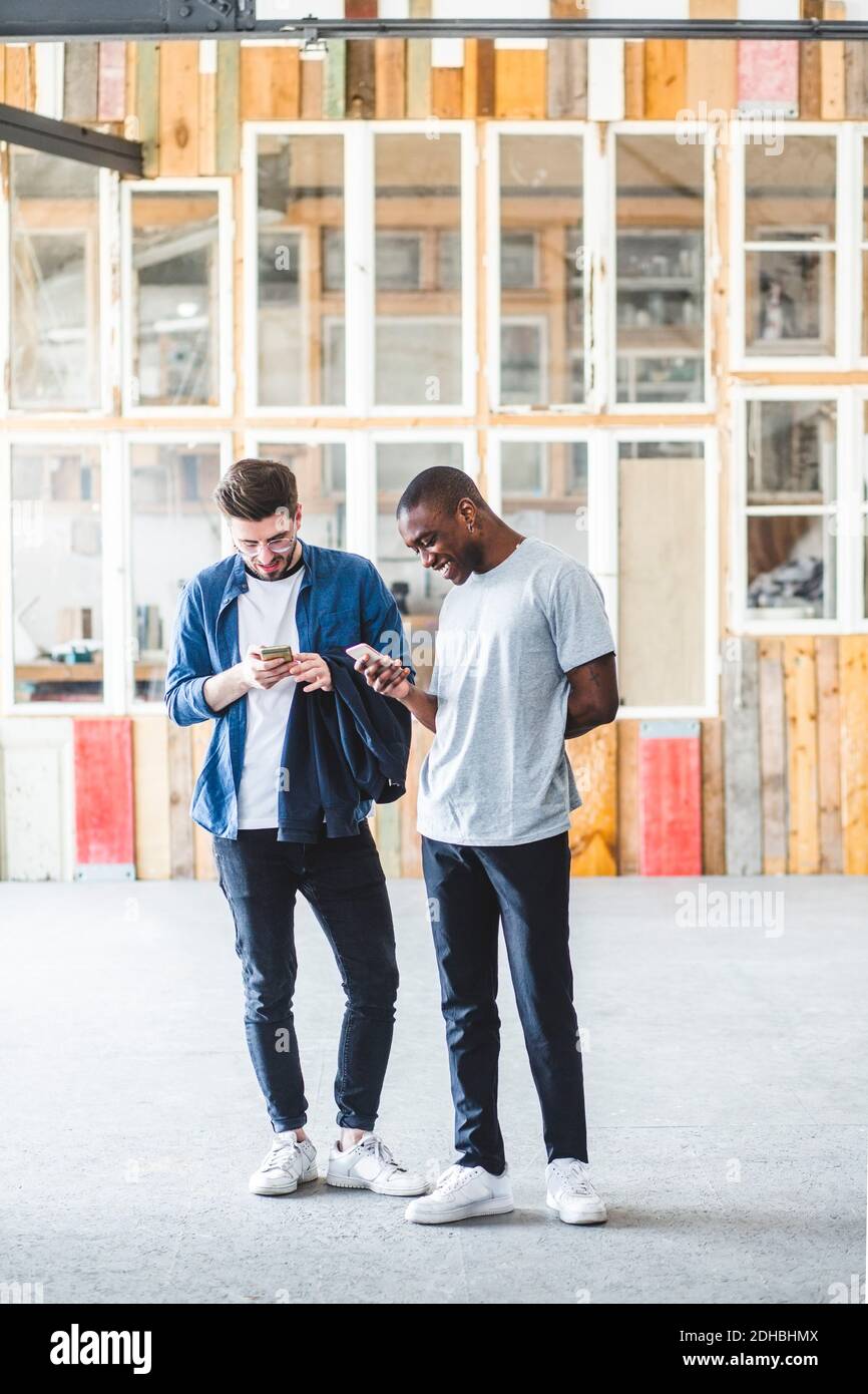 Full length of smiling businessmen text messaging using mobile phones at creative workplace Stock Photo