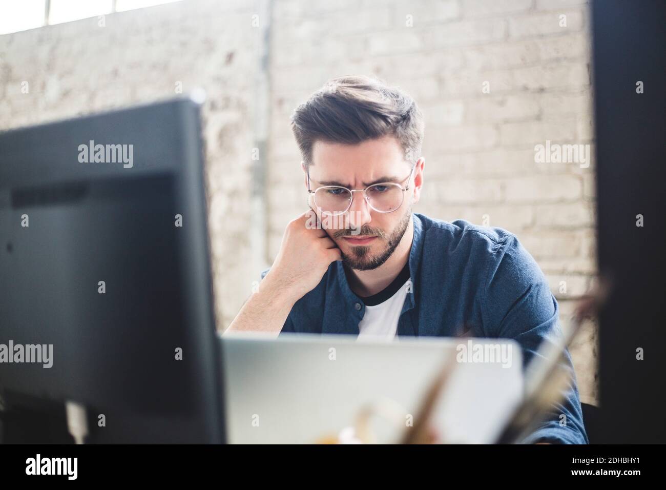 Male IT professional thinking while working on computer codes in laptop at workplace Stock Photo