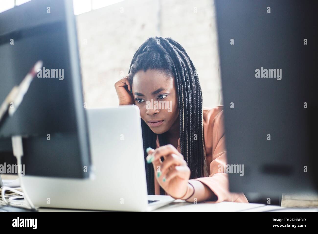 Serious female IT expert concentrating on computer codes while using laptop at workplace Stock Photo