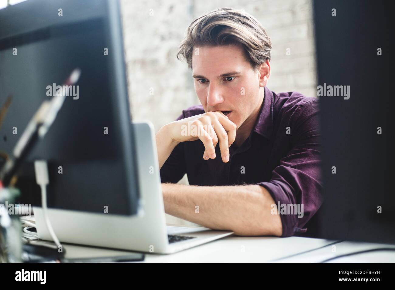 Serious male IT professional thinking while coding in laptop at creative workplace Stock Photo
