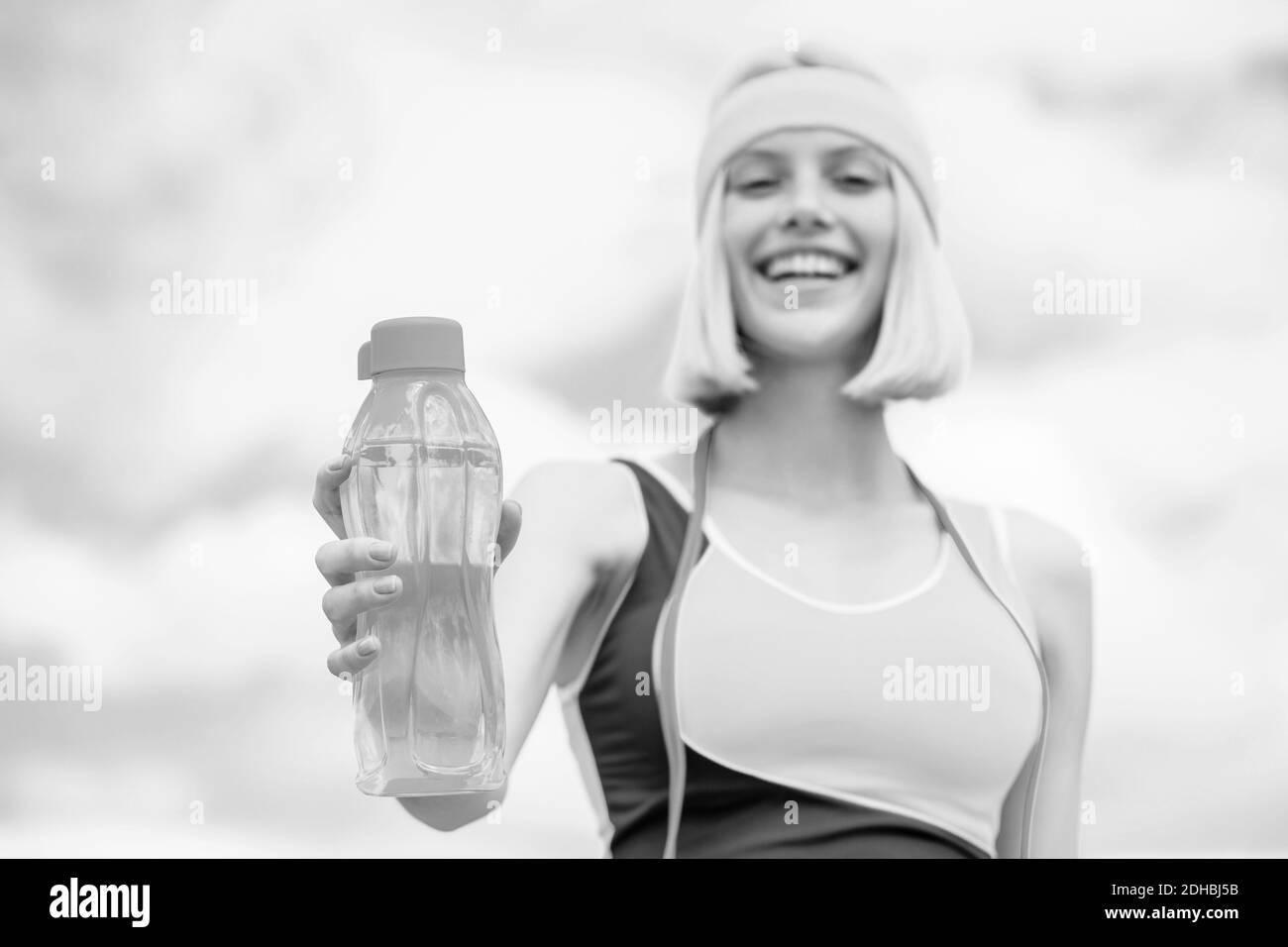 Sports girl drinks water from a bottle on a sky background. Drinking during sport. Black and white Stock Photo