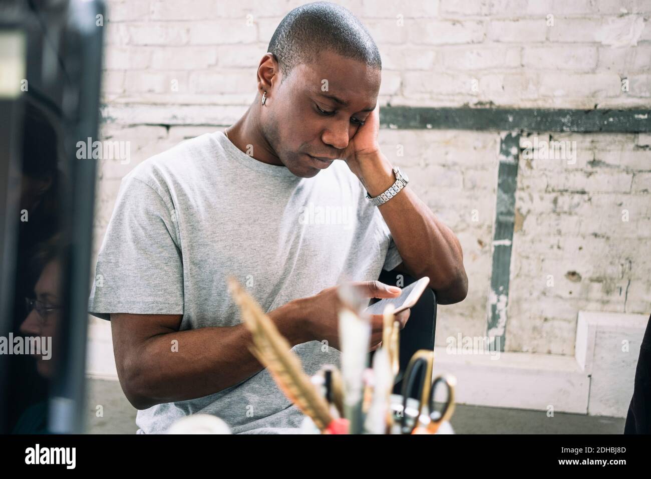 Young male hacker using smart phone while sitting at creative workplace Stock Photo