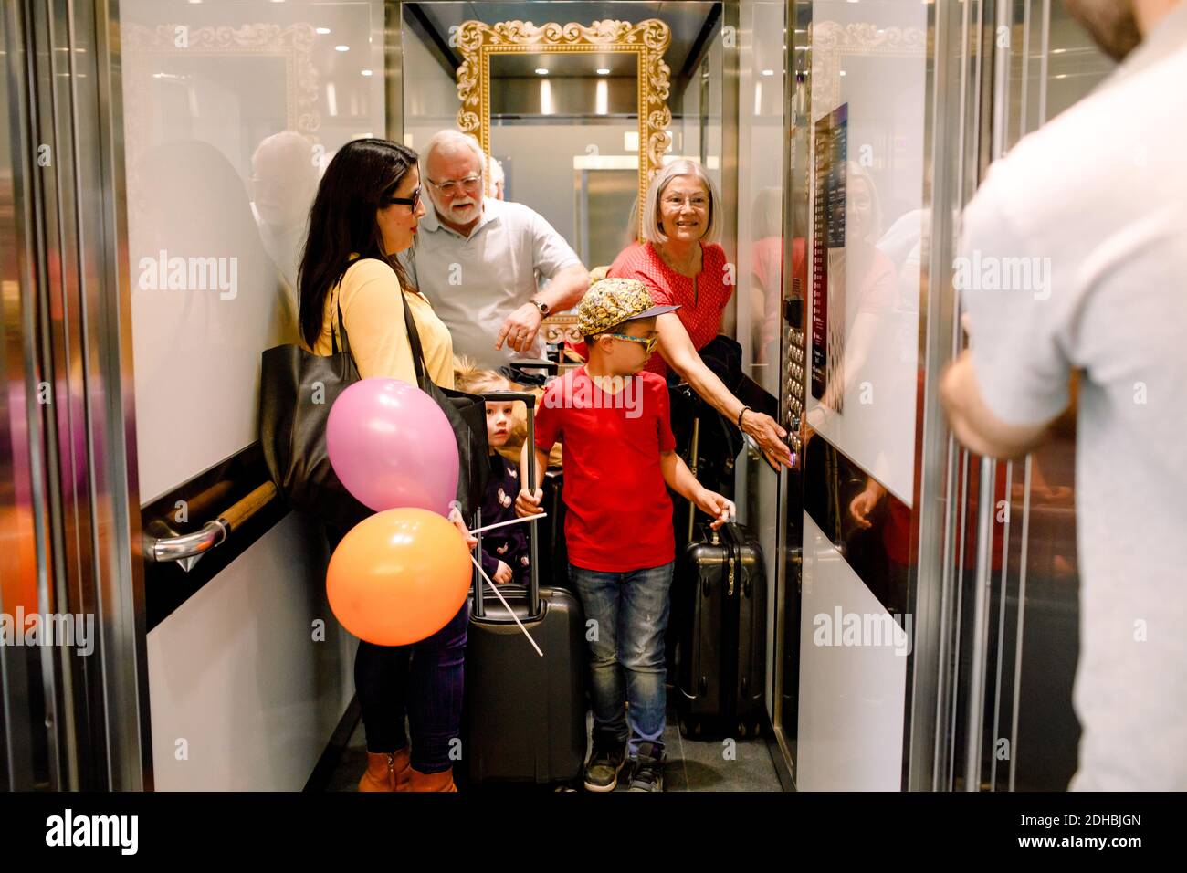 Woman pressing button in elevator while standing with family Stock Photo