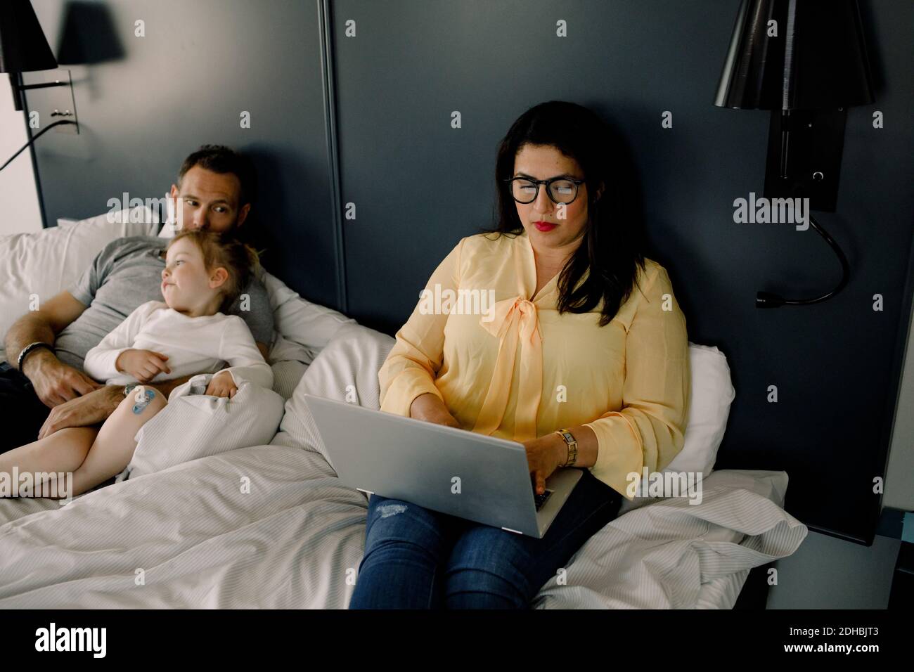 High angle view of woman using laptop while sitting by man and daughter on bed Stock Photo