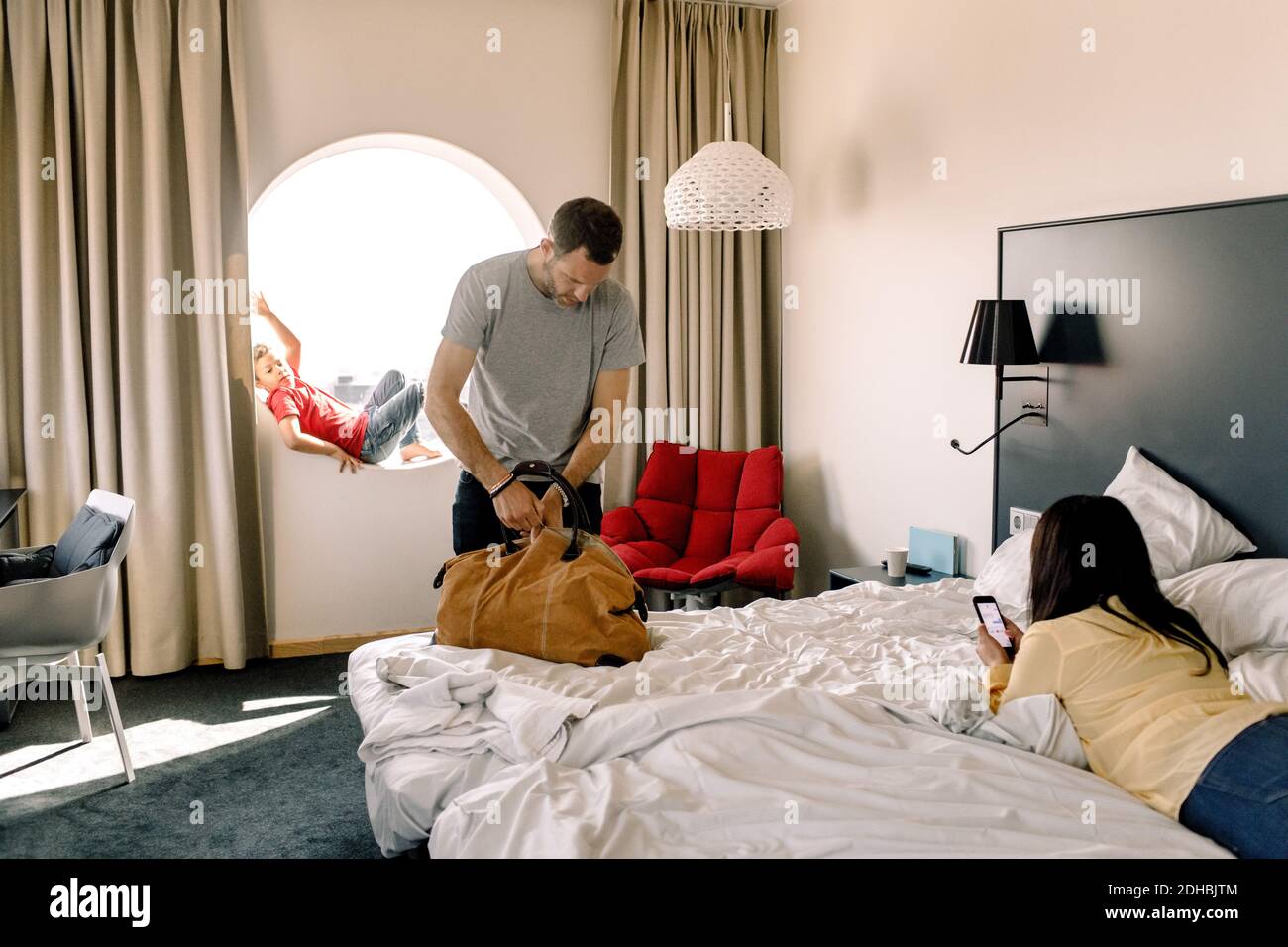 Man packing bag while woman using phone on bed in hotel Stock Photo
