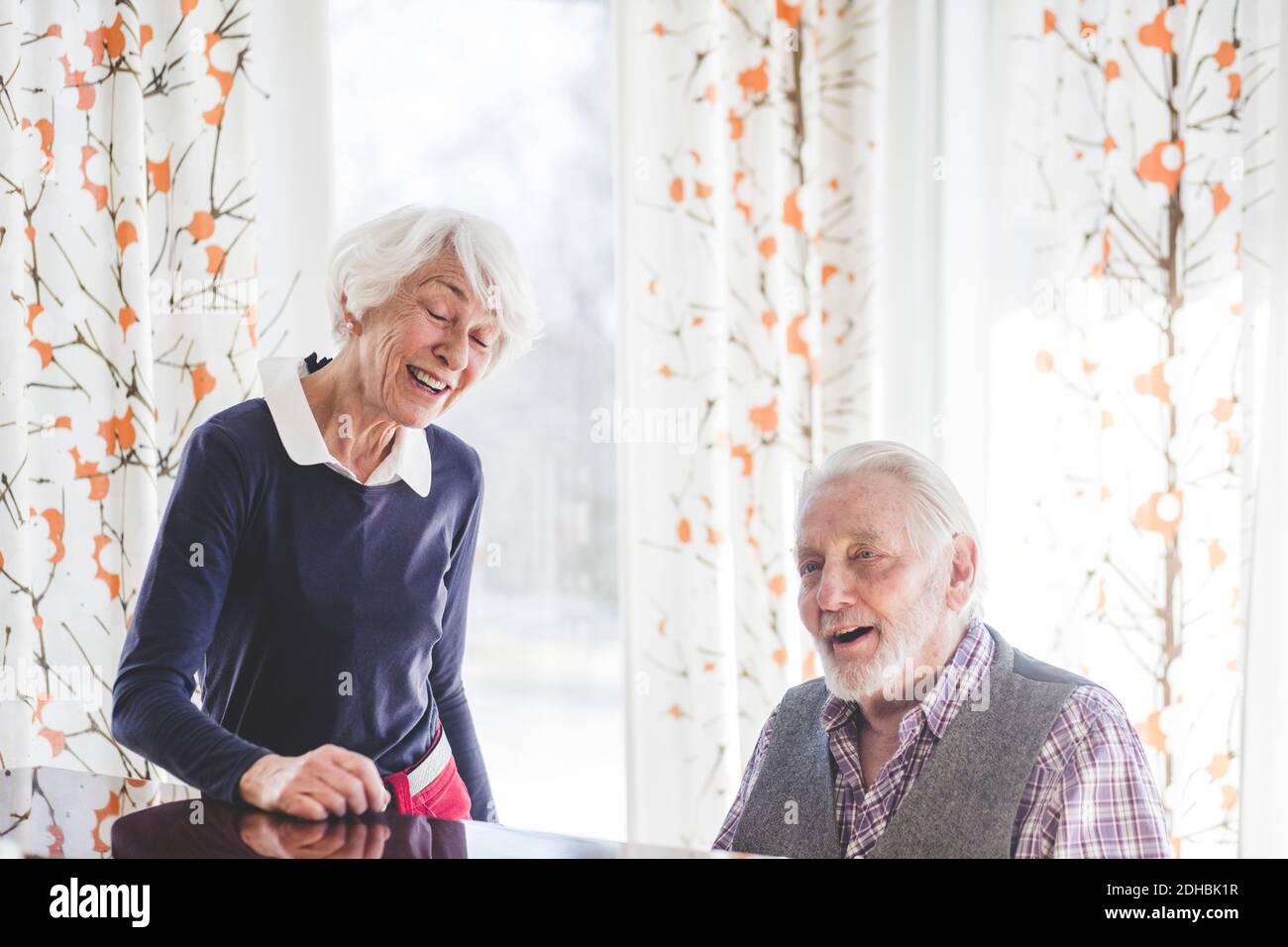 Senior man playing piano while woman singing in nursing home Stock
