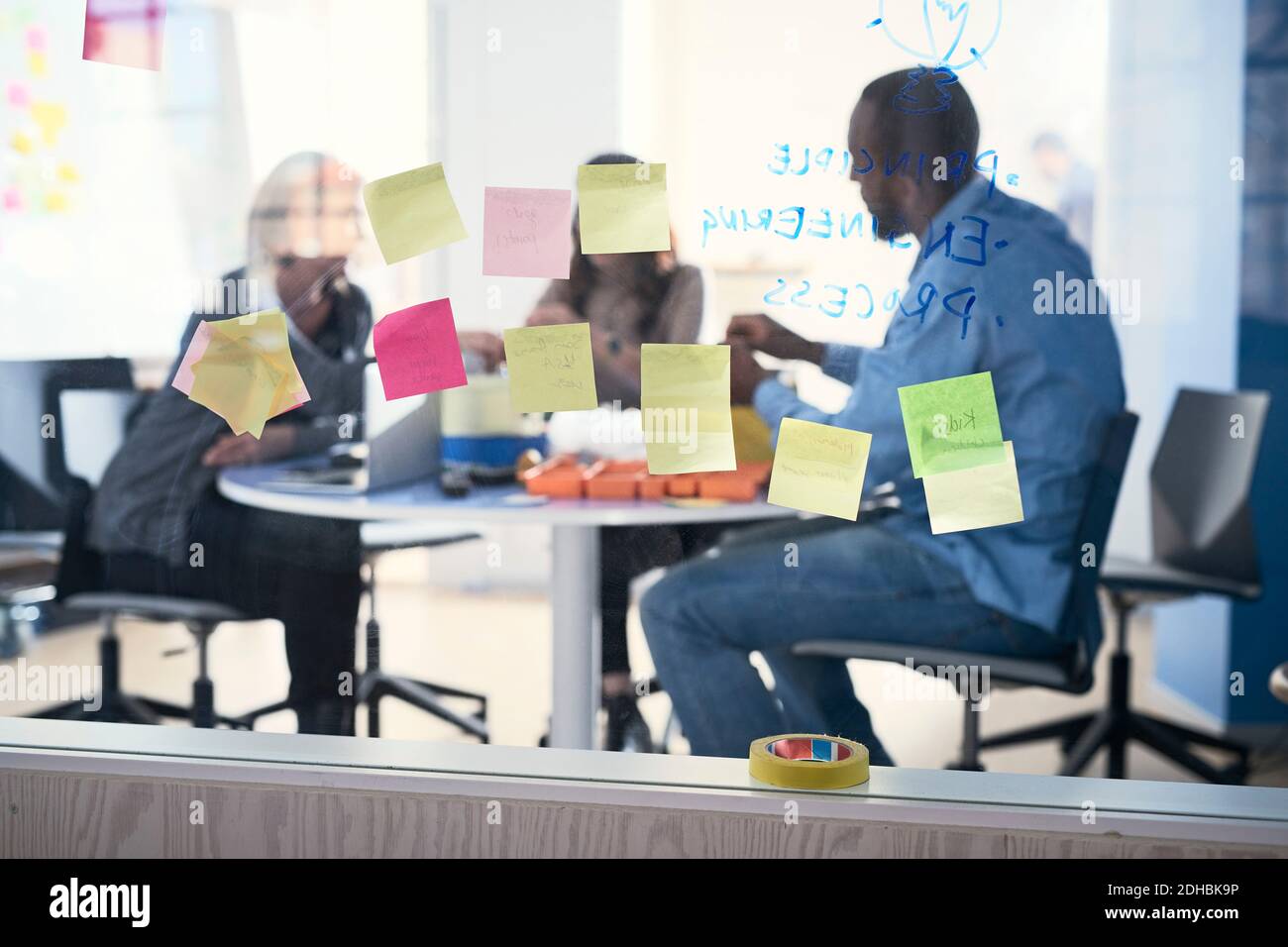 Adhesive notes stuck on glass while business professionals working in background Stock Photo