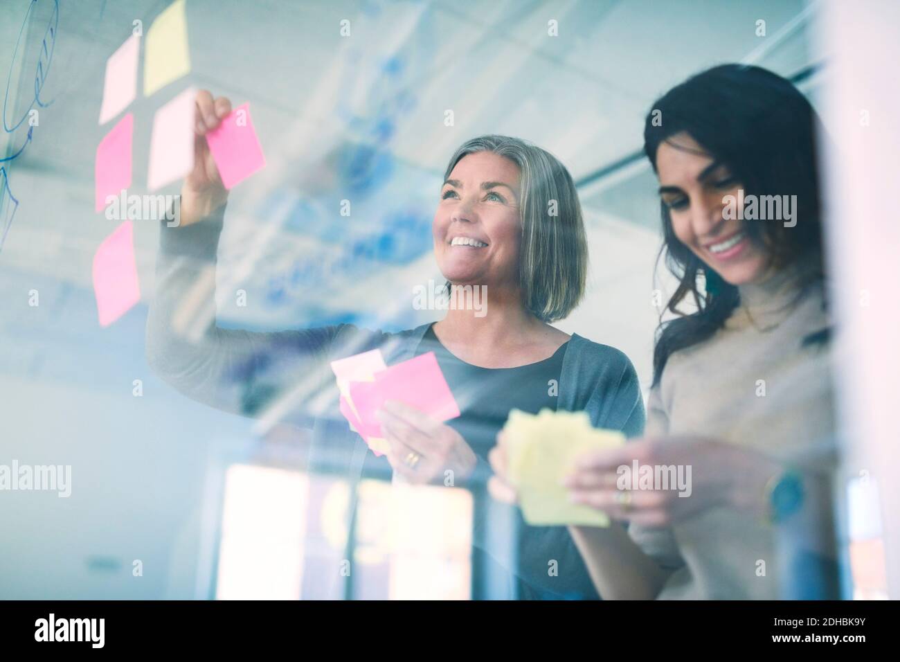 Low angle view of business professionals smiling while sticking adhesive notes on glass in office Stock Photo