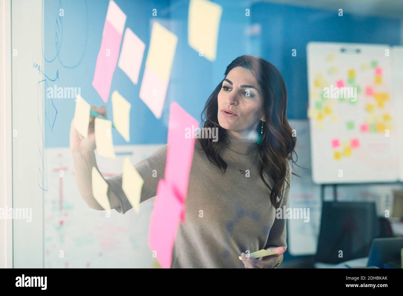 Female mature engineer writing on adhesive note stuck to glass in office Stock Photo