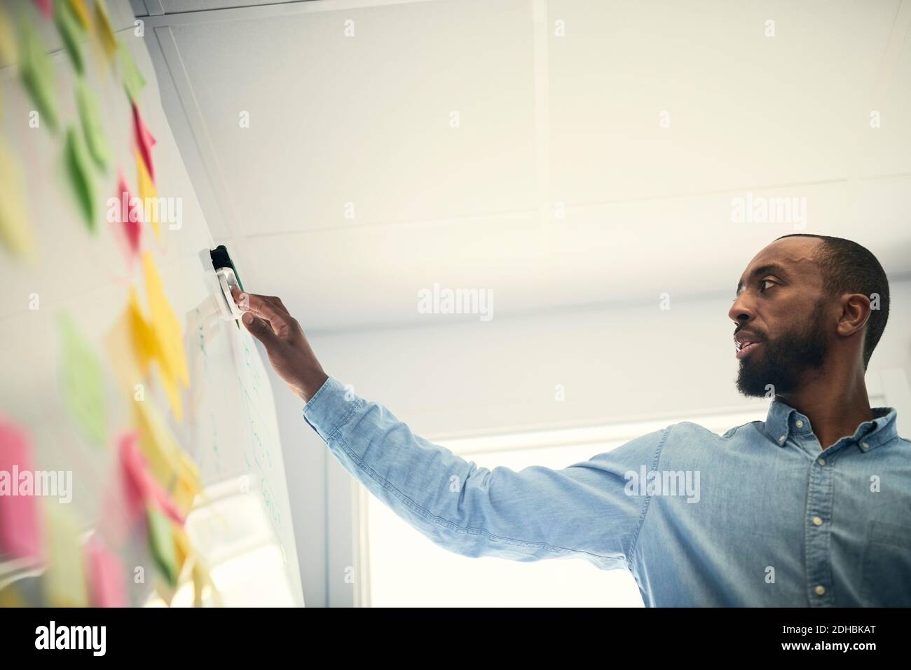 Low angle view of male engineer reading adhesive notes stuck on whiteboard in office Stock Photo