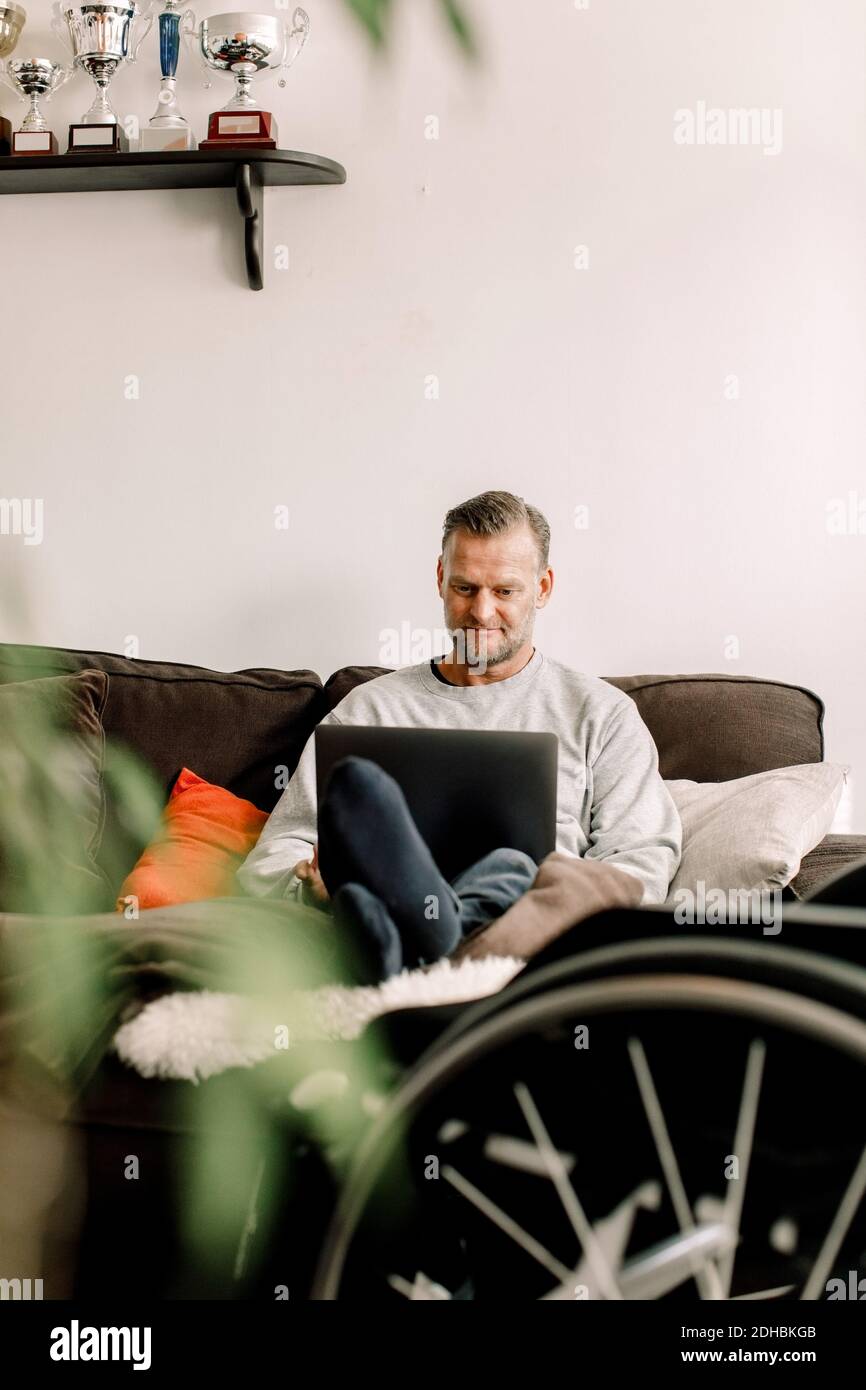 Disabled mature man using laptop while sitting on sofa at home Stock Photo