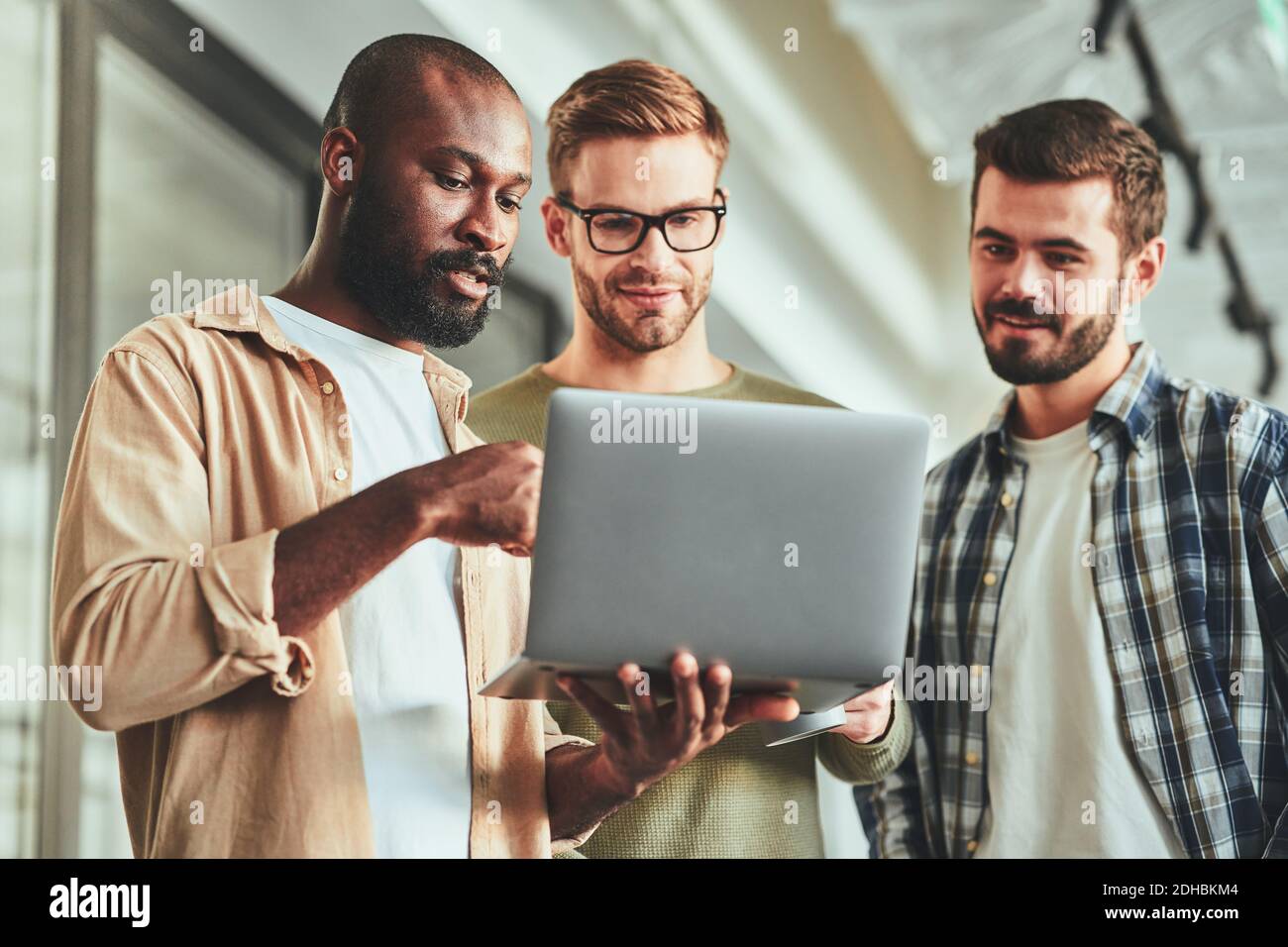 Three multiracial male colleagues looking at laptop screen Stock Photo