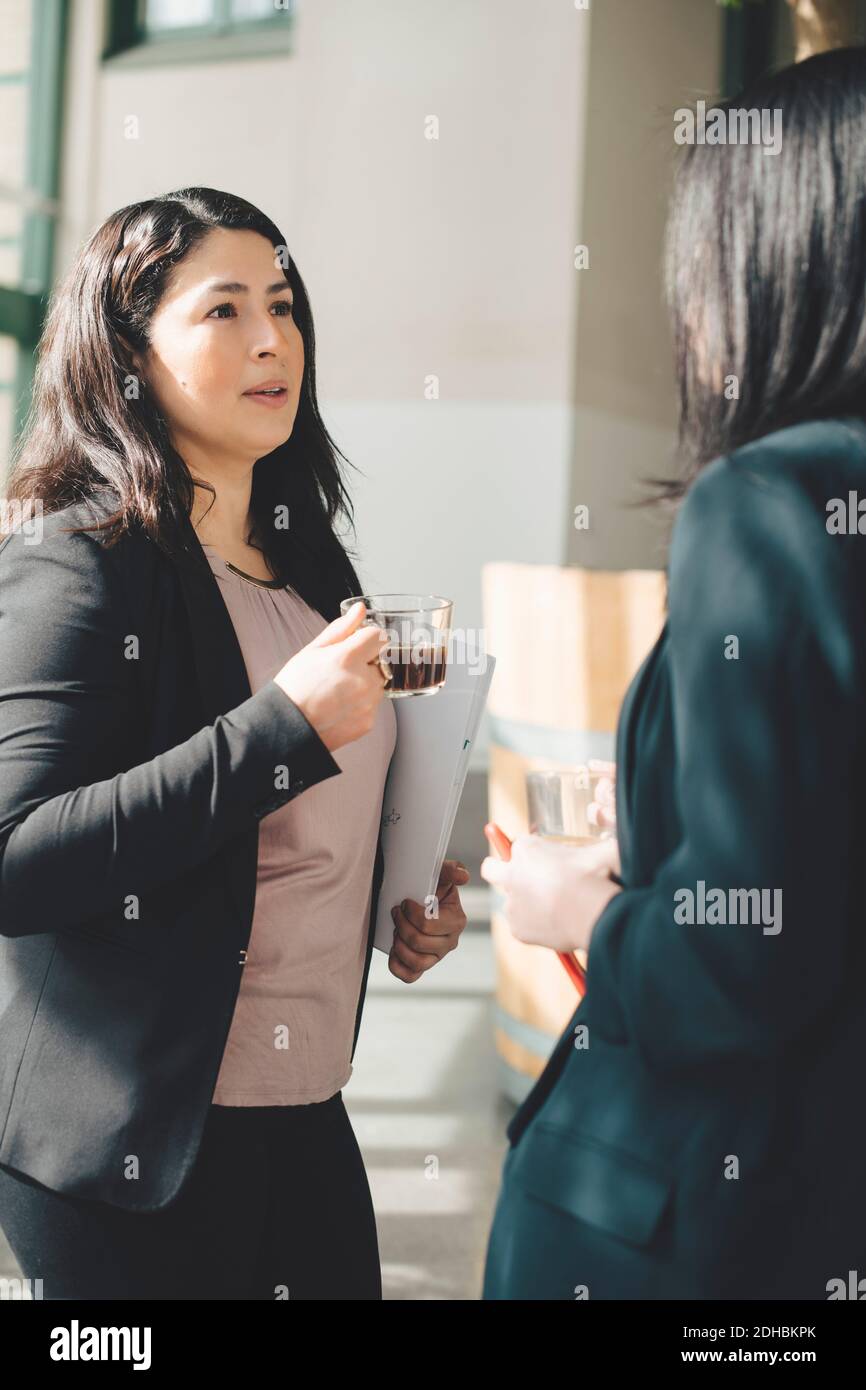 Female professionals having coffee while discussing in office corridor Stock Photo