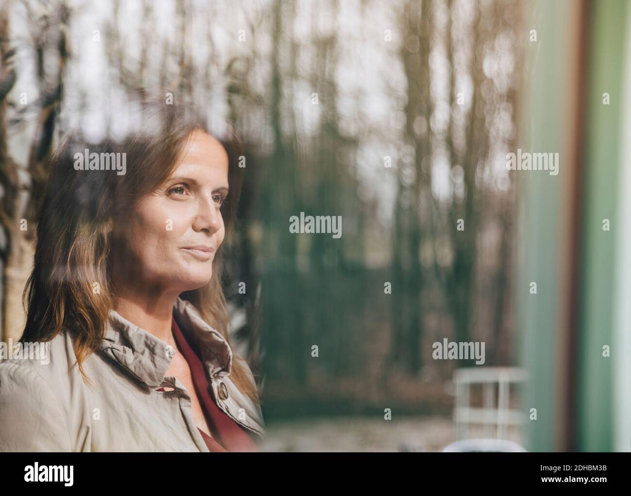 Smiling mature female professional thinking while looking through window at office Stock Photo