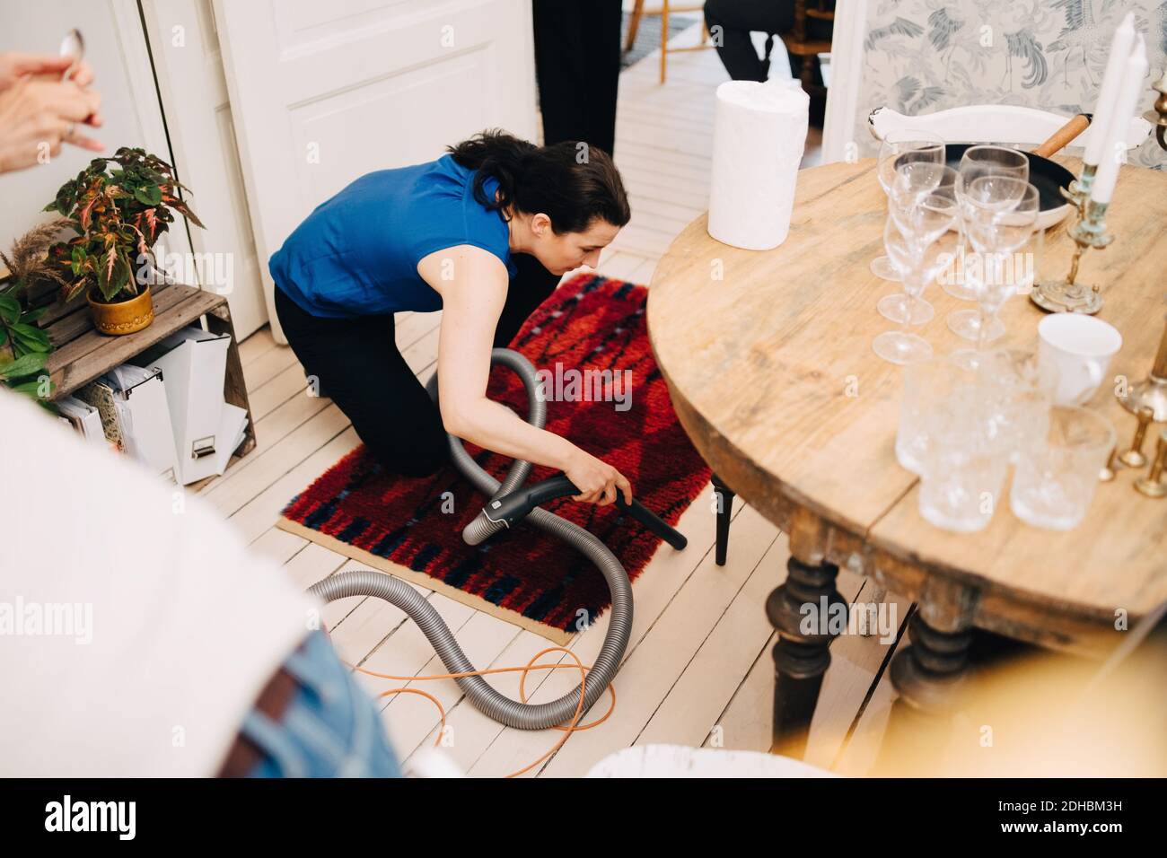 High angle view of mature woman cleaning hardwood floor with vacuum cleaner after party at home Stock Photo