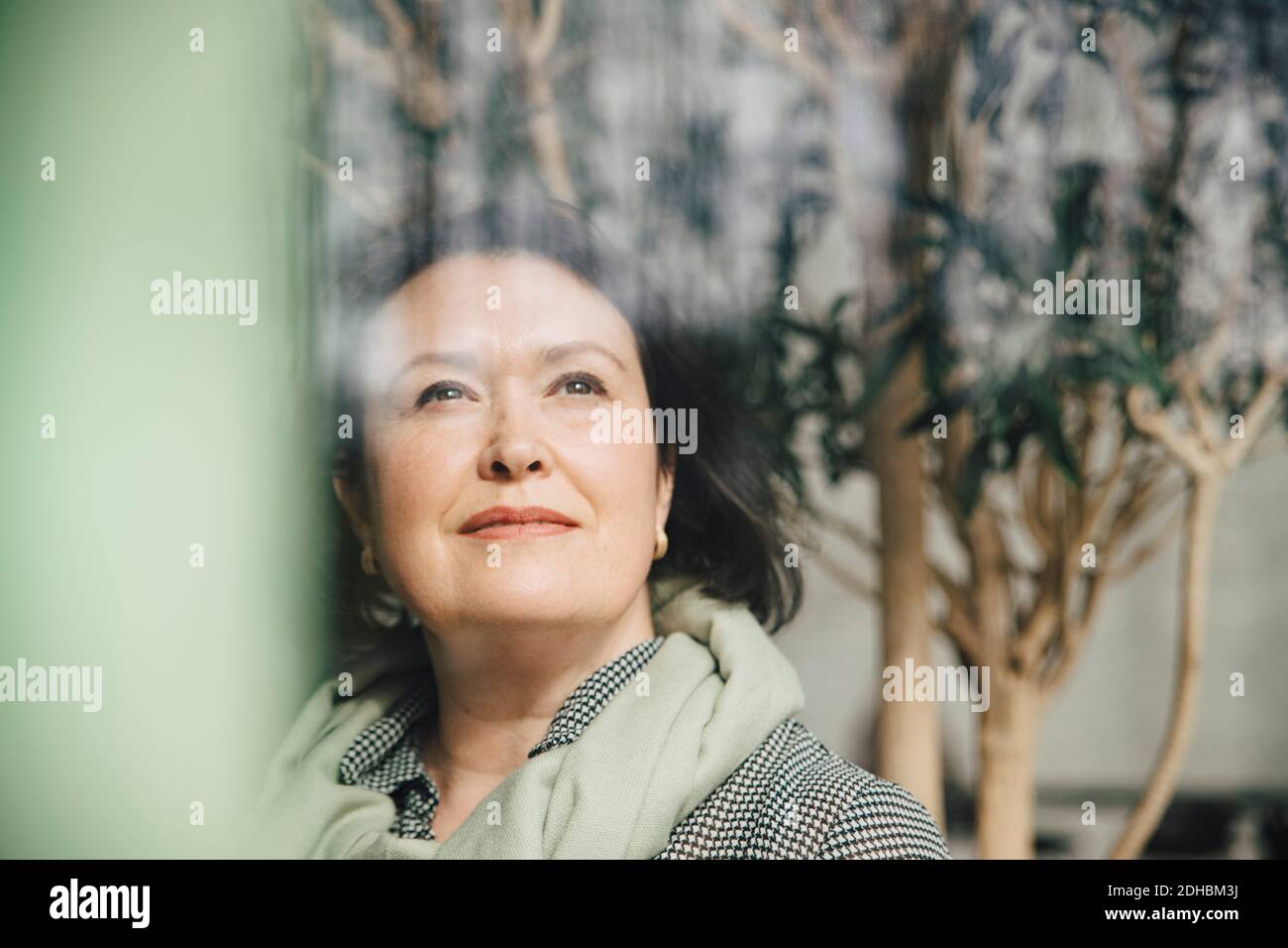Mature businesswoman thinking while looking through window at workplace Stock Photo