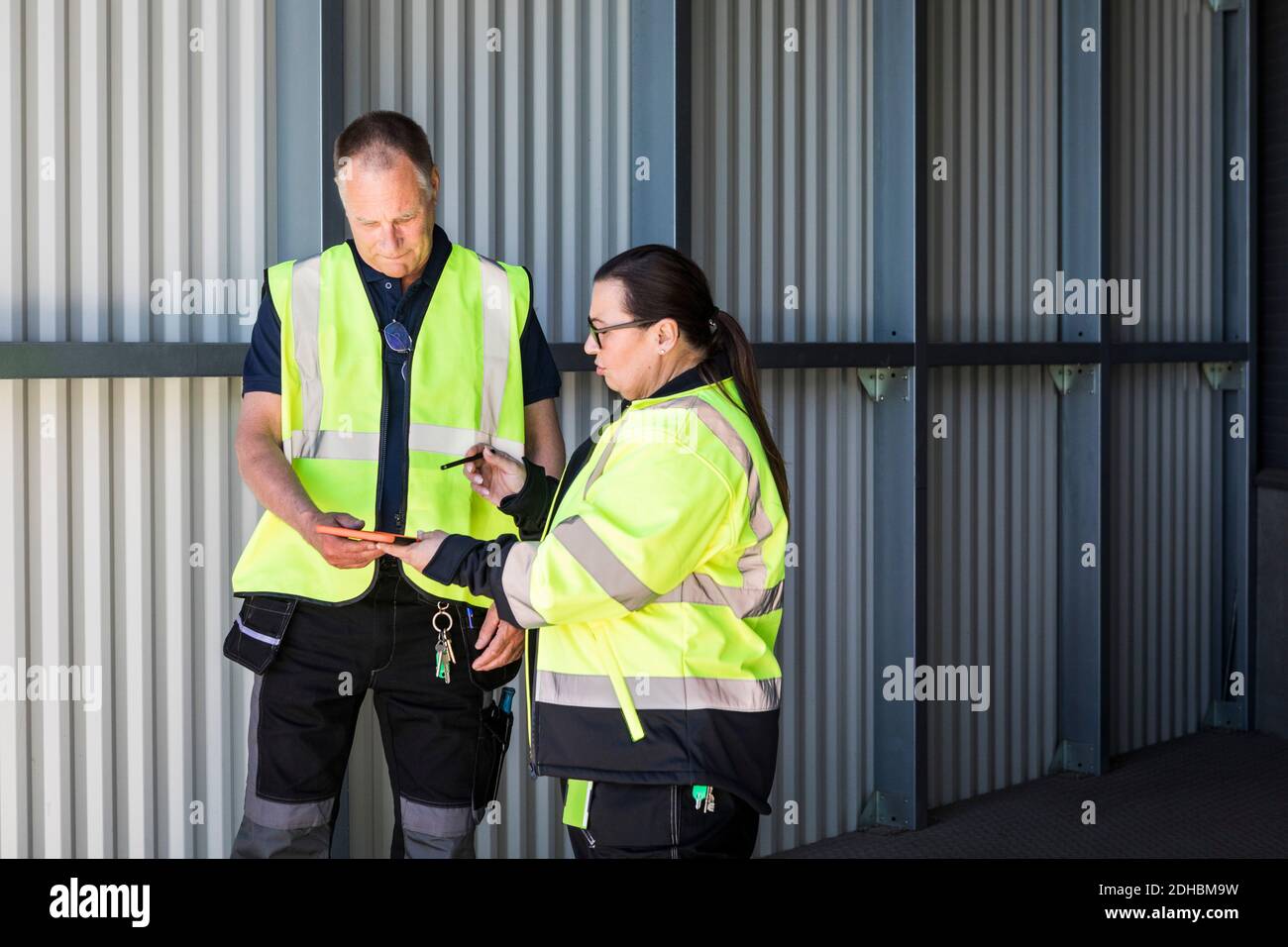Warehouse workers discussing over digital tablet while standing at entrance Stock Photo