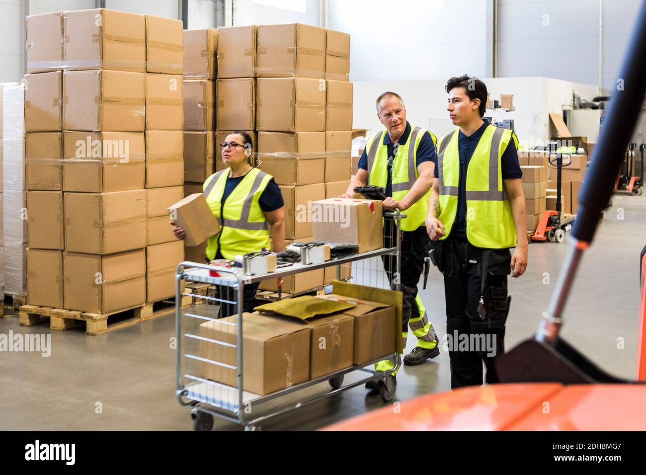 Multi-ethnic coworkers pushing cart at distribution warehouse Stock Photo