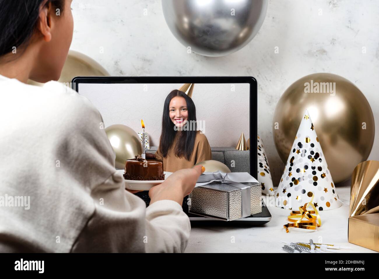 Young woman celebrating birthday online in quarantine time using video call with friend holding cupcake with candle. Remote Celebration Concept Stock Photo