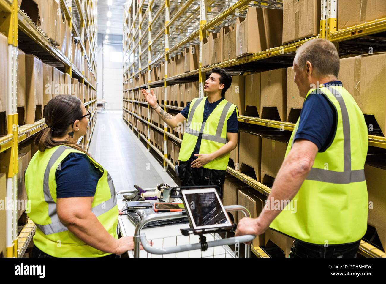 Worker Distribution Young worker discussing with coworkers with cart while standing on ...