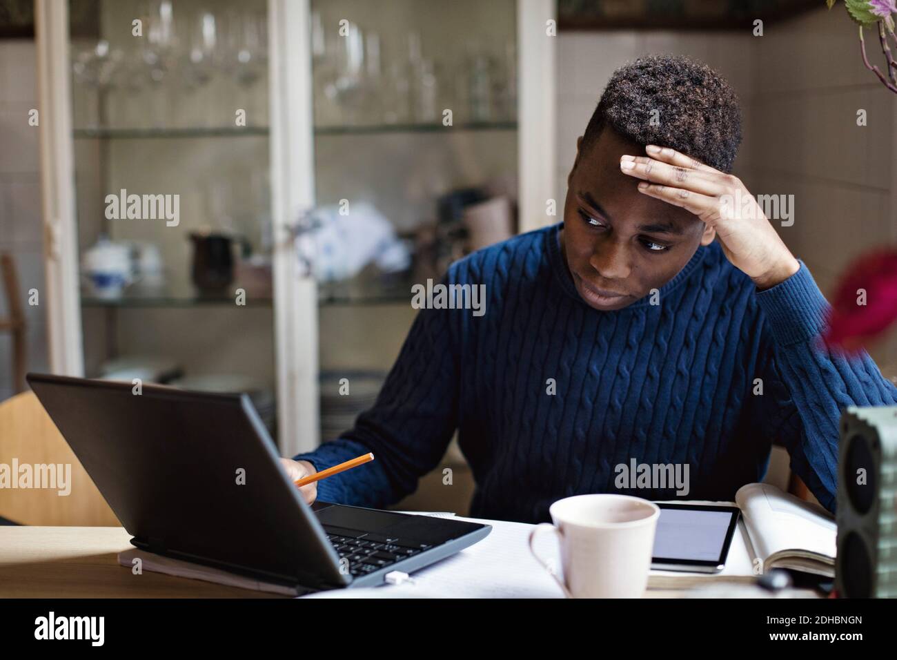 Worried teenage boy looking at laptop while doing homework on table Stock Photo