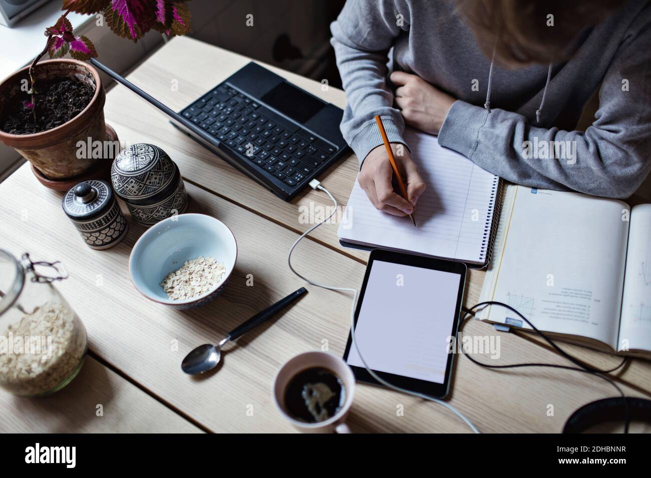 High angle view of teenage boy writing on book while using digital tablet for homework Stock Photo