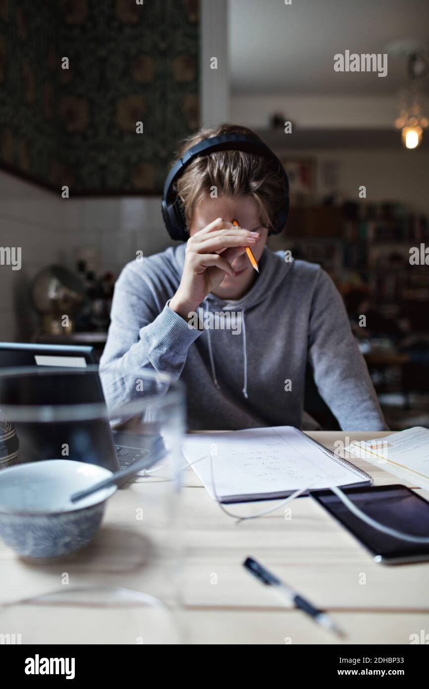 Teenage boy reading book while using headphones at home Stock Photo