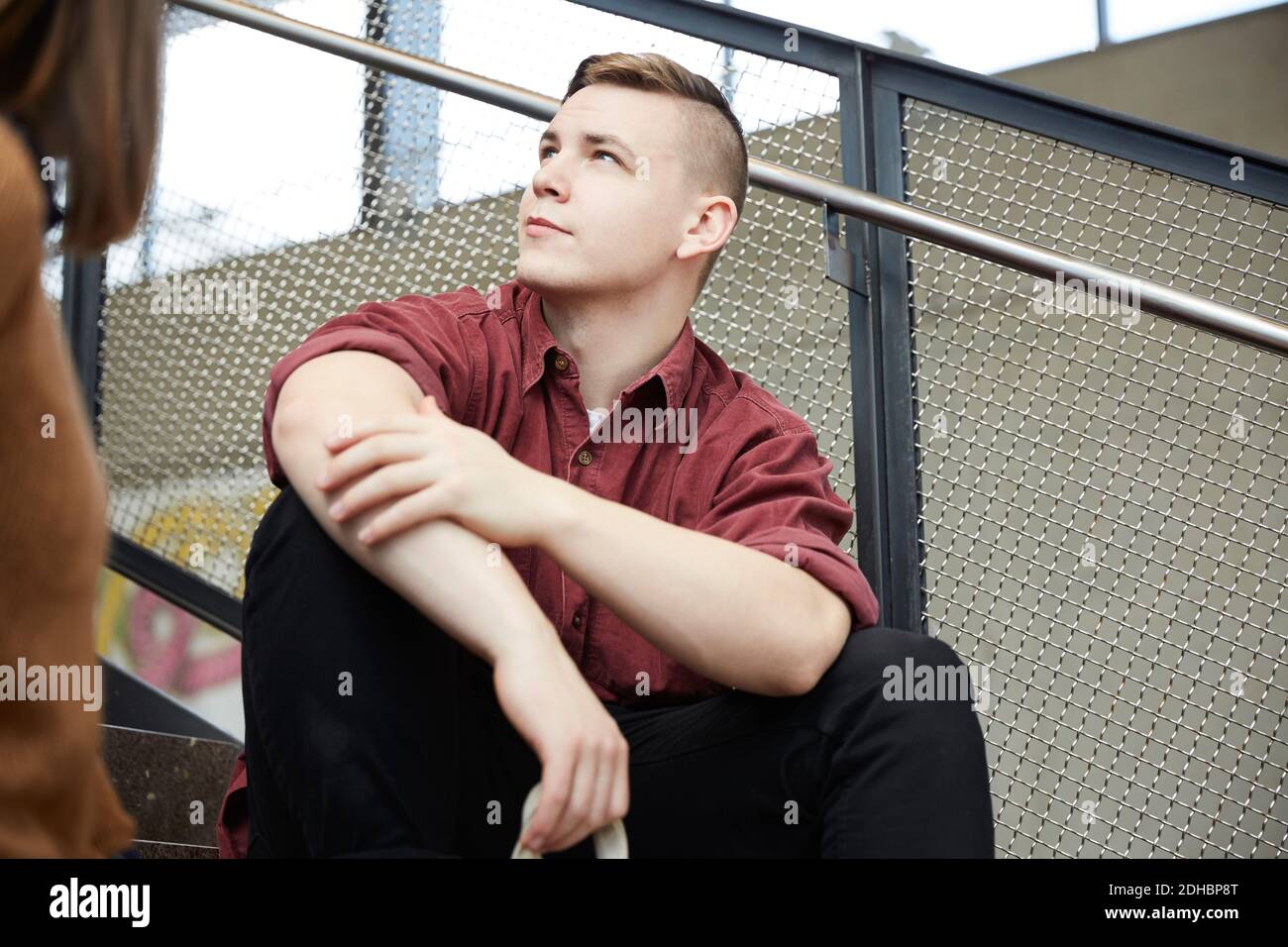 Young man looking away while sitting on steps against railing at university Stock Photo