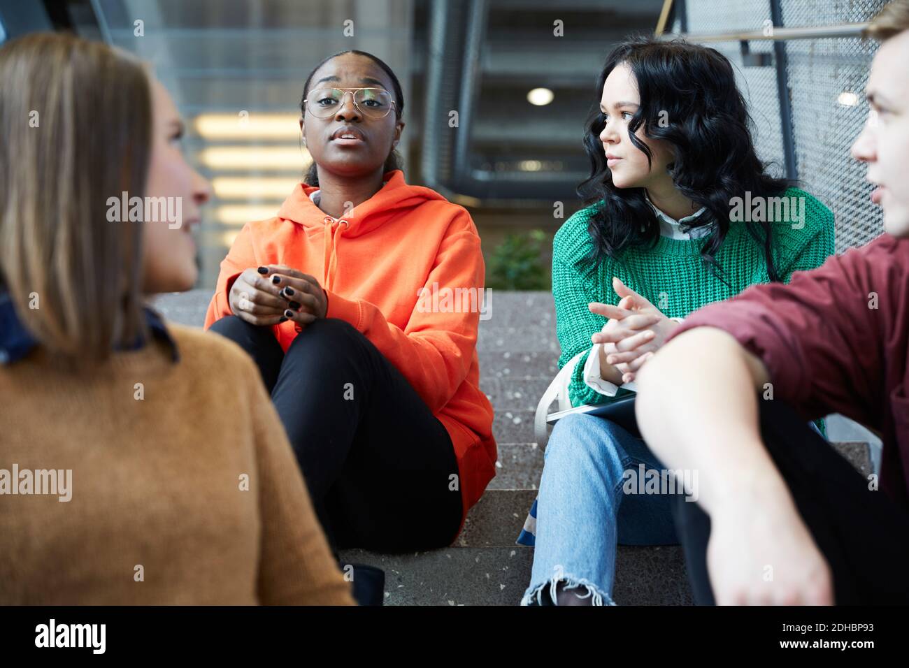 Multi-ethnic students talking while sitting on steps at university Stock Photo