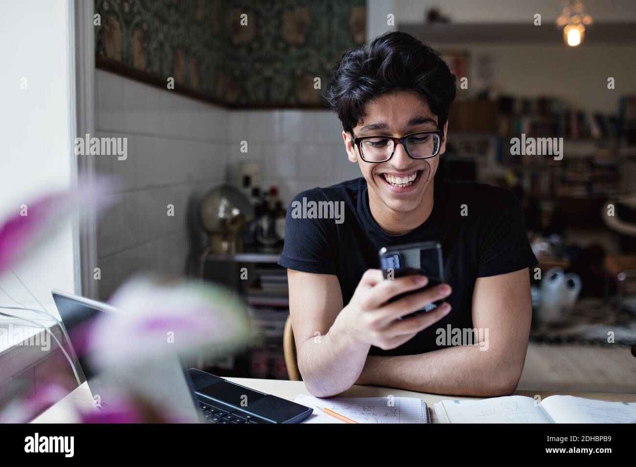 Smiling young man using social media while doing homework at home Stock Photo