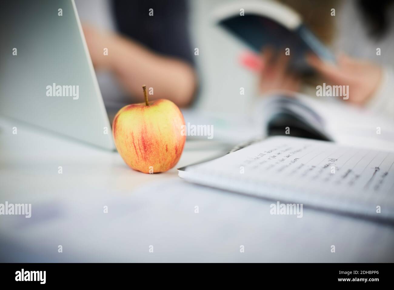 Close-up of apple by laptop and book on table in university Stock Photo