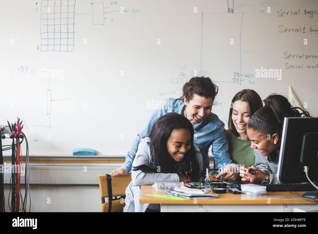 Smiling female teacher and high school teenage students preparing robot on desk in classroom Stock Photo
