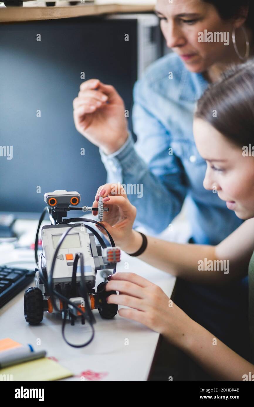 Female teacher assisting teenage student preparing robot on desk in classroom at high school Stock Photo