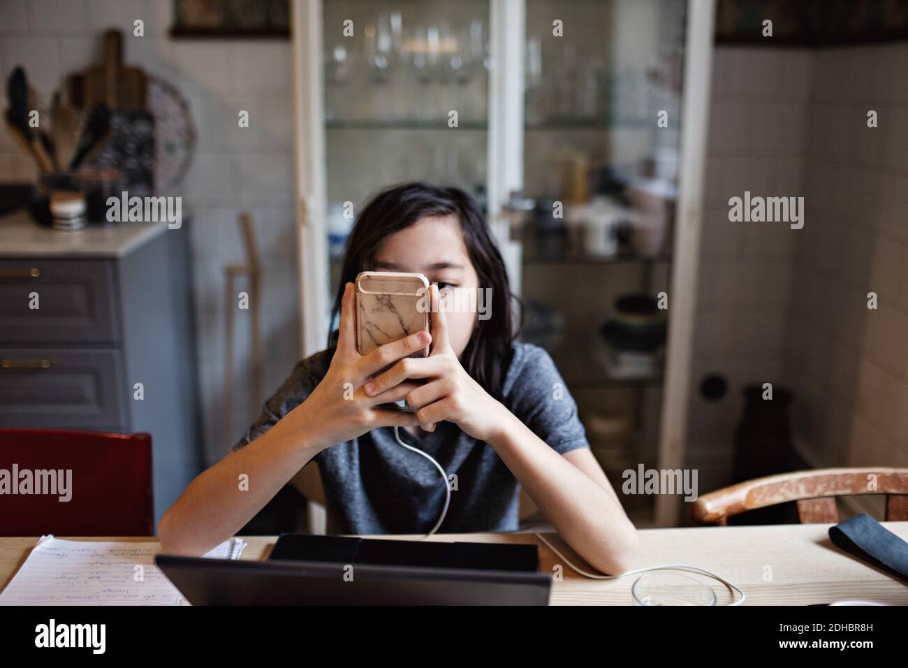 Boy using smart phone while doing homework at home Stock Photo