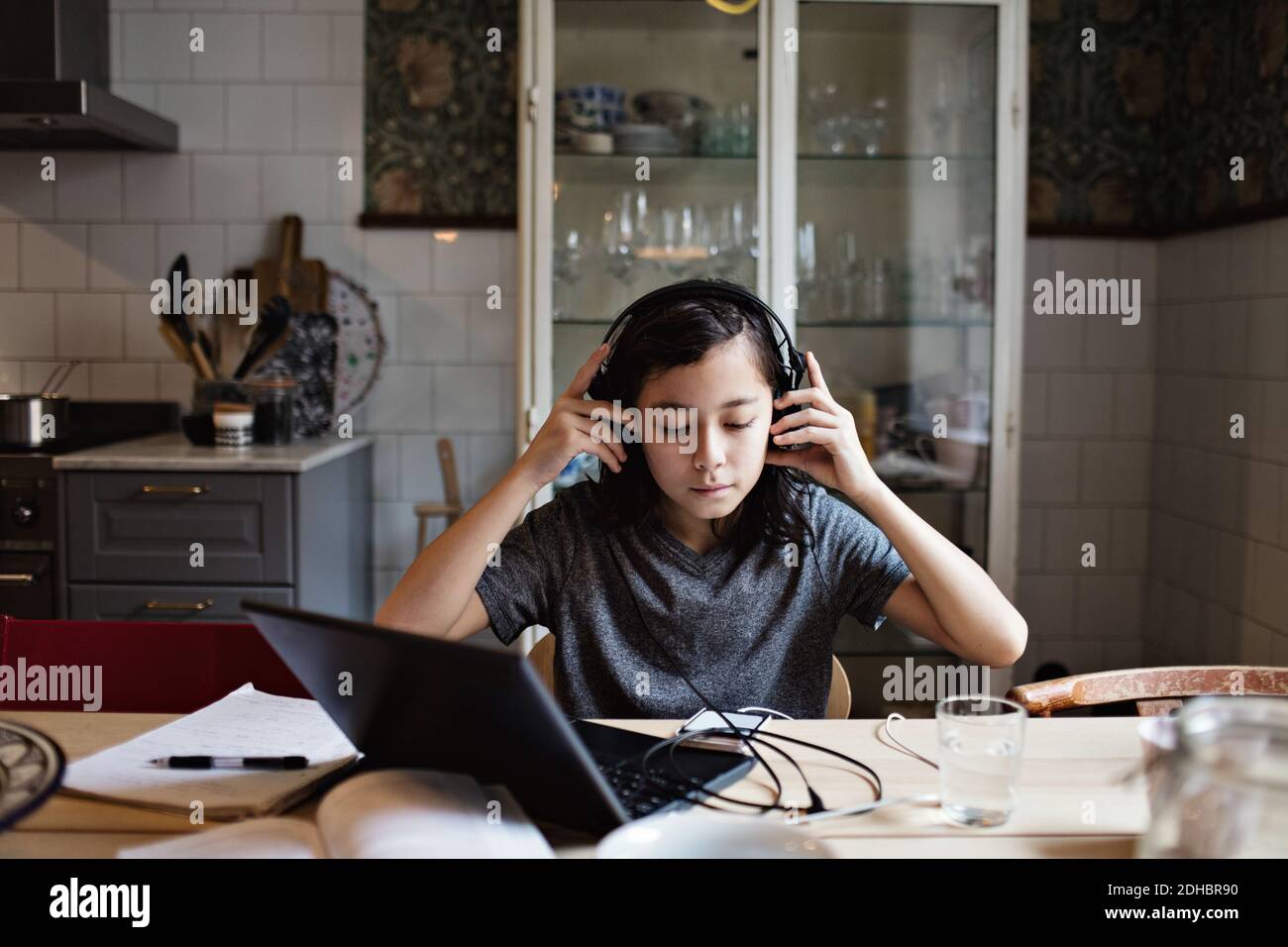 Boy using headphones while doing homework at home Stock Photo