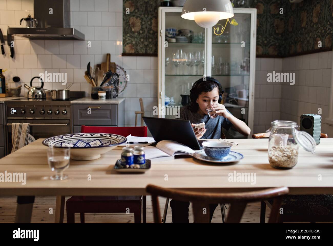 Boy drinking water while using laptop for homework at home Stock Photo