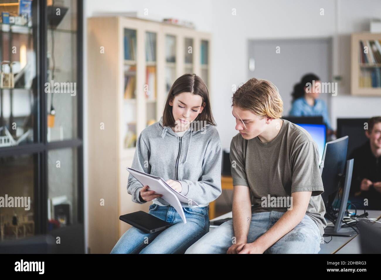 High school students studying from book while sitting on desk in computer lab Stock Photo