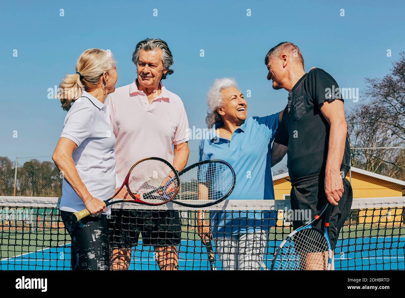 Happy male and female seniors greeting while standing at tennis court against clear sky Stock Photo