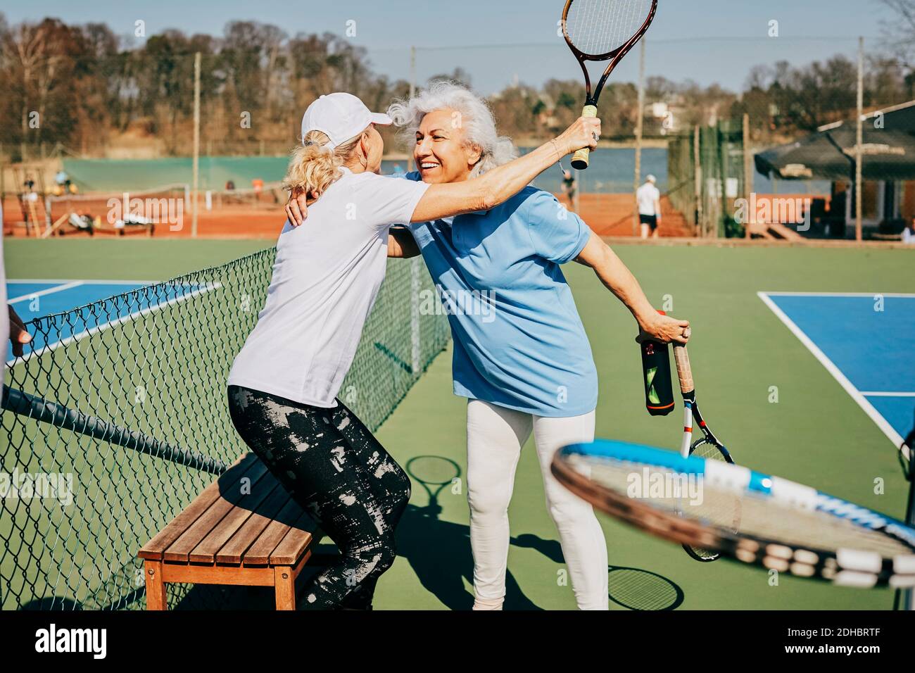 Happy female senior friends greeting at tennis court during summer Stock Photo