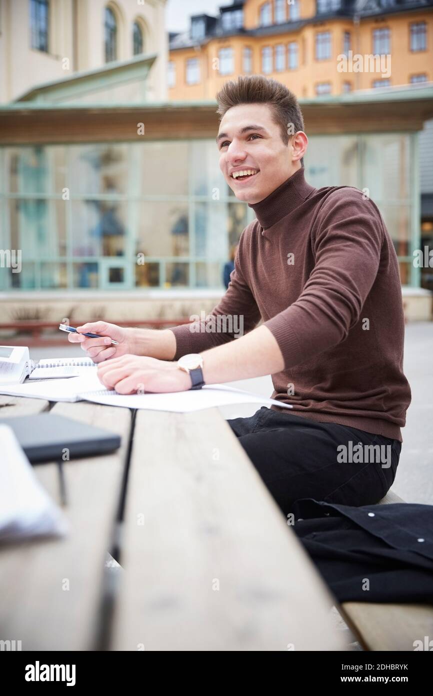 Smiling teenage boy looking away while sitting at table in schoolyard Stock Photo