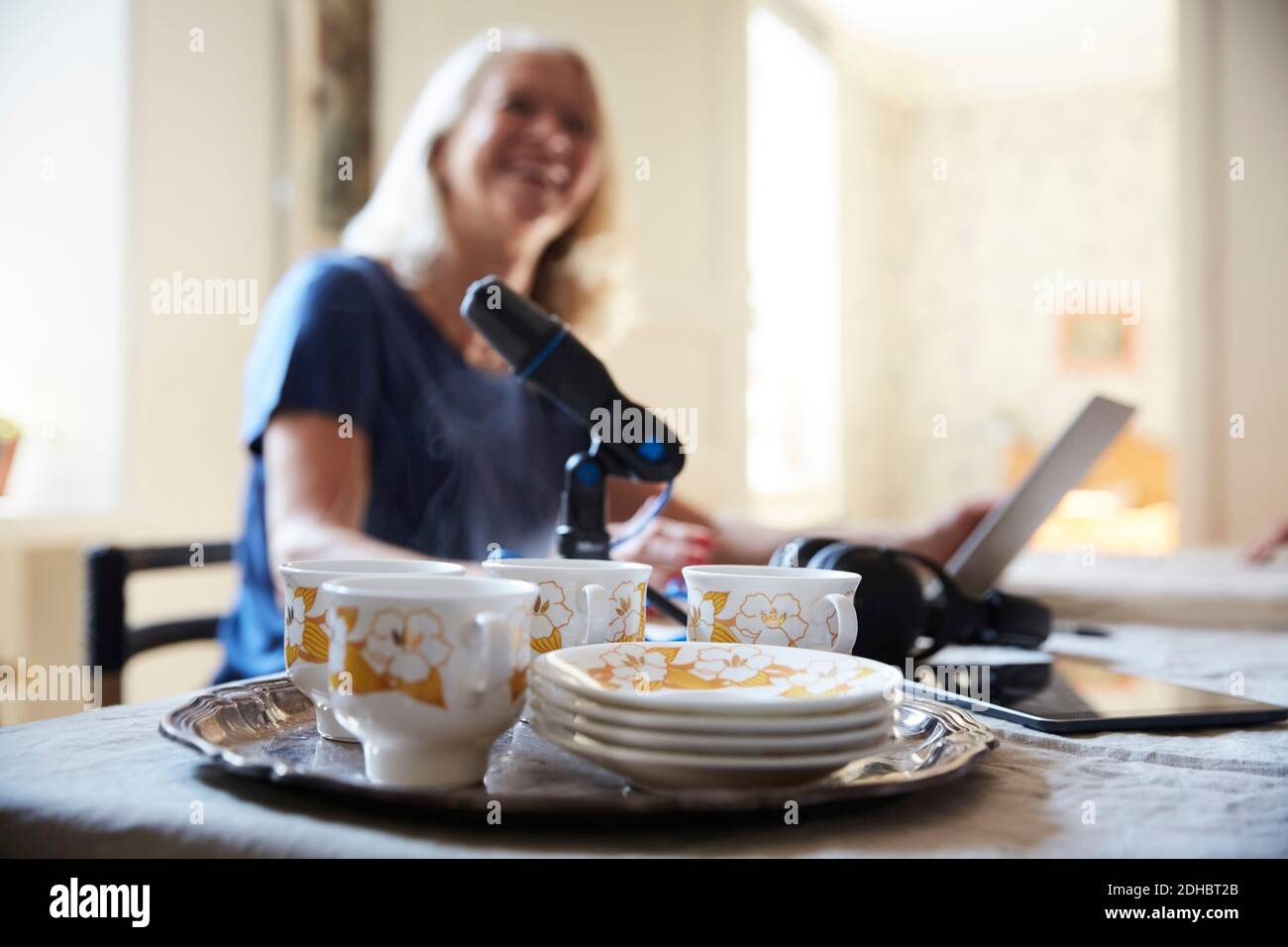 Close-up of crockery and microphone with woman sitting in background at home Stock Photo