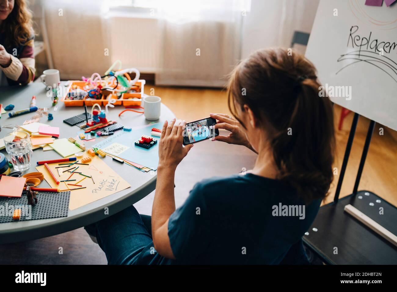 High angle rear view of businesswoman photographing stationery on table at creative office Stock Photo